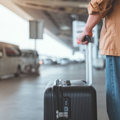 Rear view of male traveler standing with suitcase waiting for airport charter bus outside.