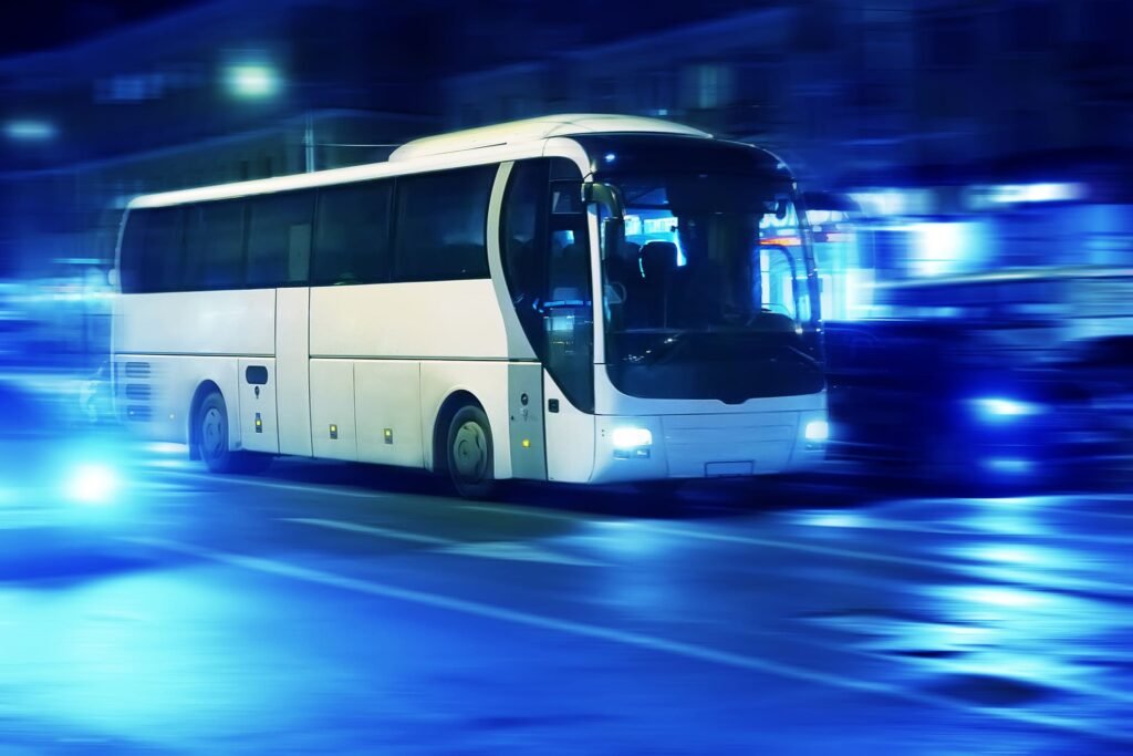 White Bus driving along a city street, illuminated by bright blue lights