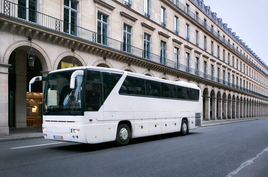 A white tourist bus for corporate groups drives along a city street.