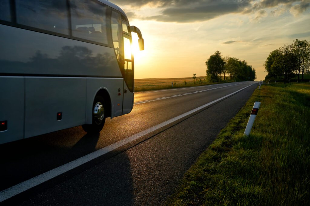 White Bus driving along the asphalt road in a rural landscape at sunset.
